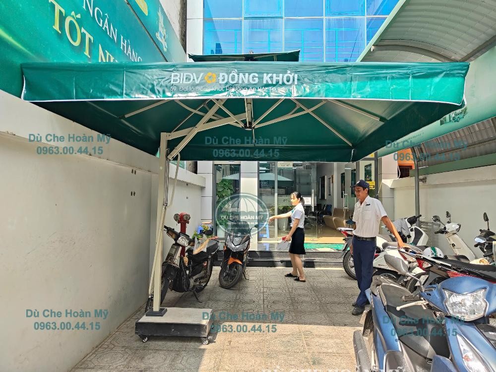 Dù in logo BIDV Đồng Khởi che khu vực có người và xe máy trước lối vào phòng giao dịch.