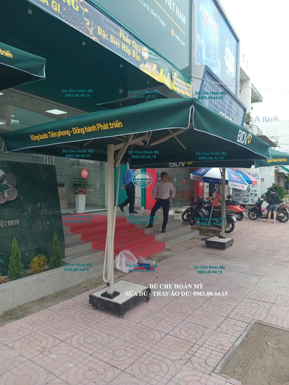 Dù lệch tâm vuông xanh in logo BIDV đặt trước mặt tiền có khu vực đỗ xe.
