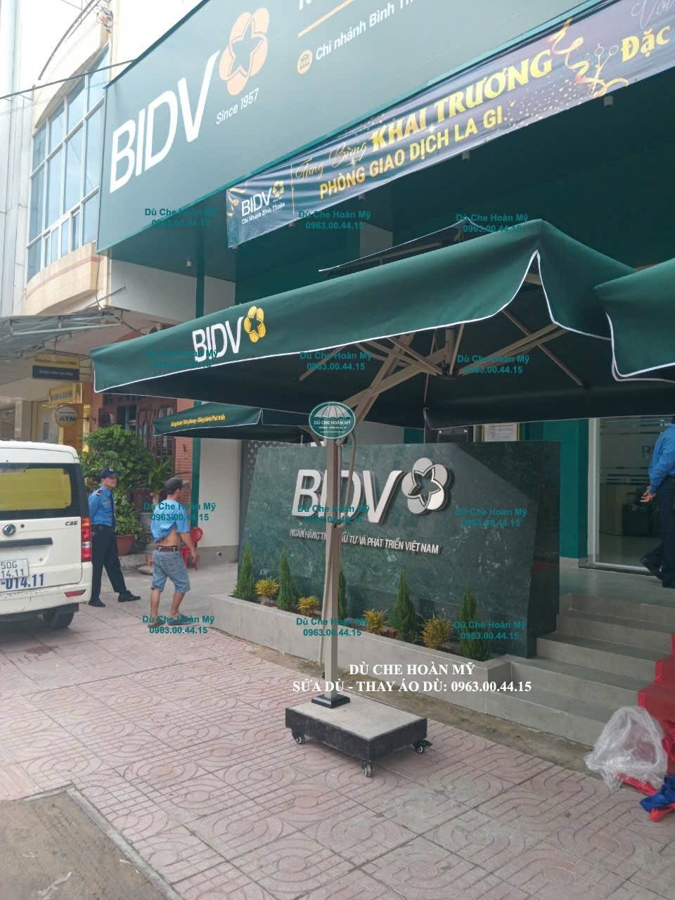 Tán dù vuông màu xanh có logo BIDV, phần tán trên và diềm tán thể hiện rõ ở góc nhìn bên.